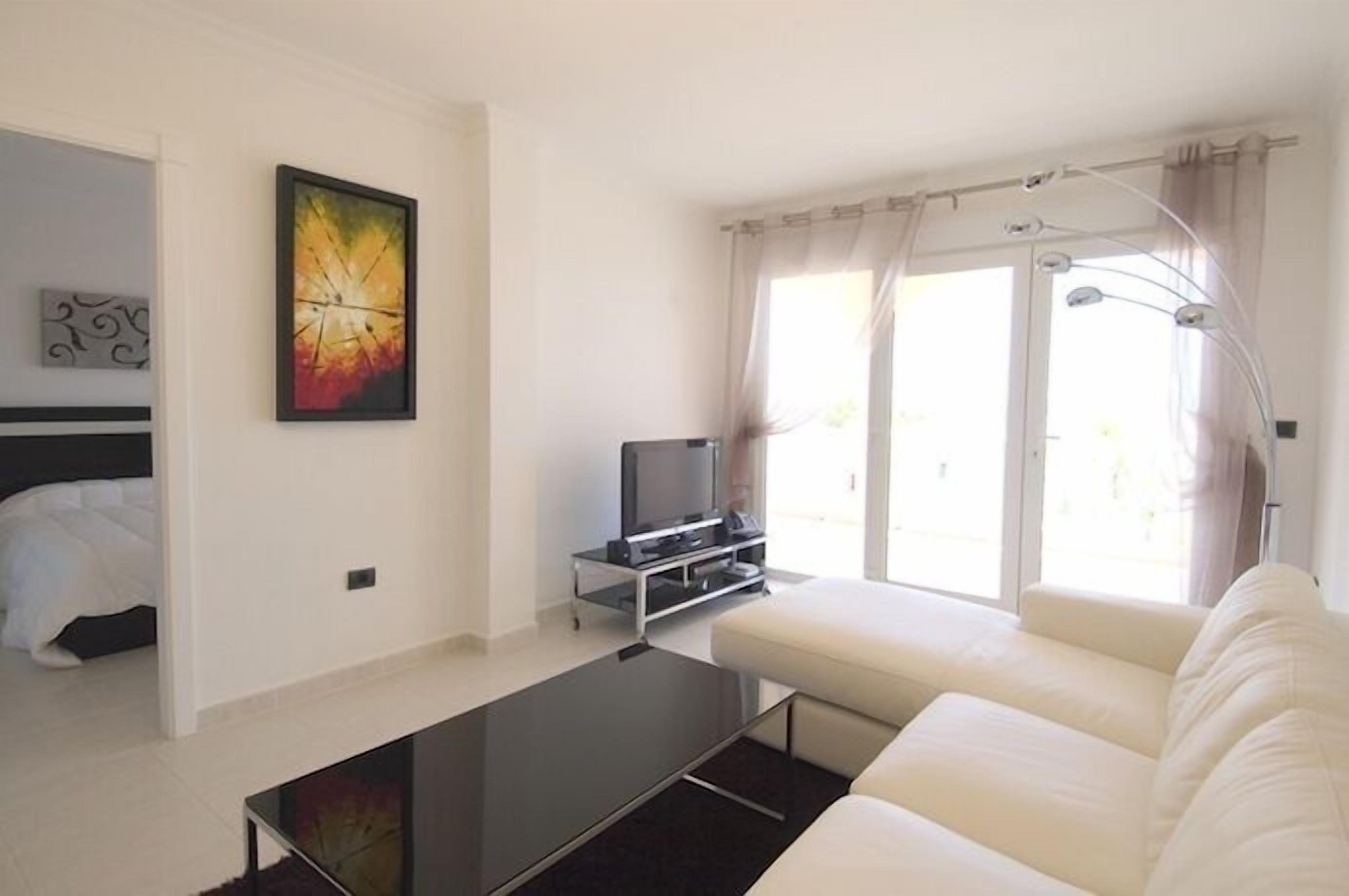 A modern living room with a sofa, a flat-screen TV, a painting, and a large window with curtains.