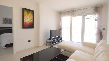 Een moderne woonkamer met een bank, een flatscreen televisie, een schilderij en een groot raam met gordijnen.