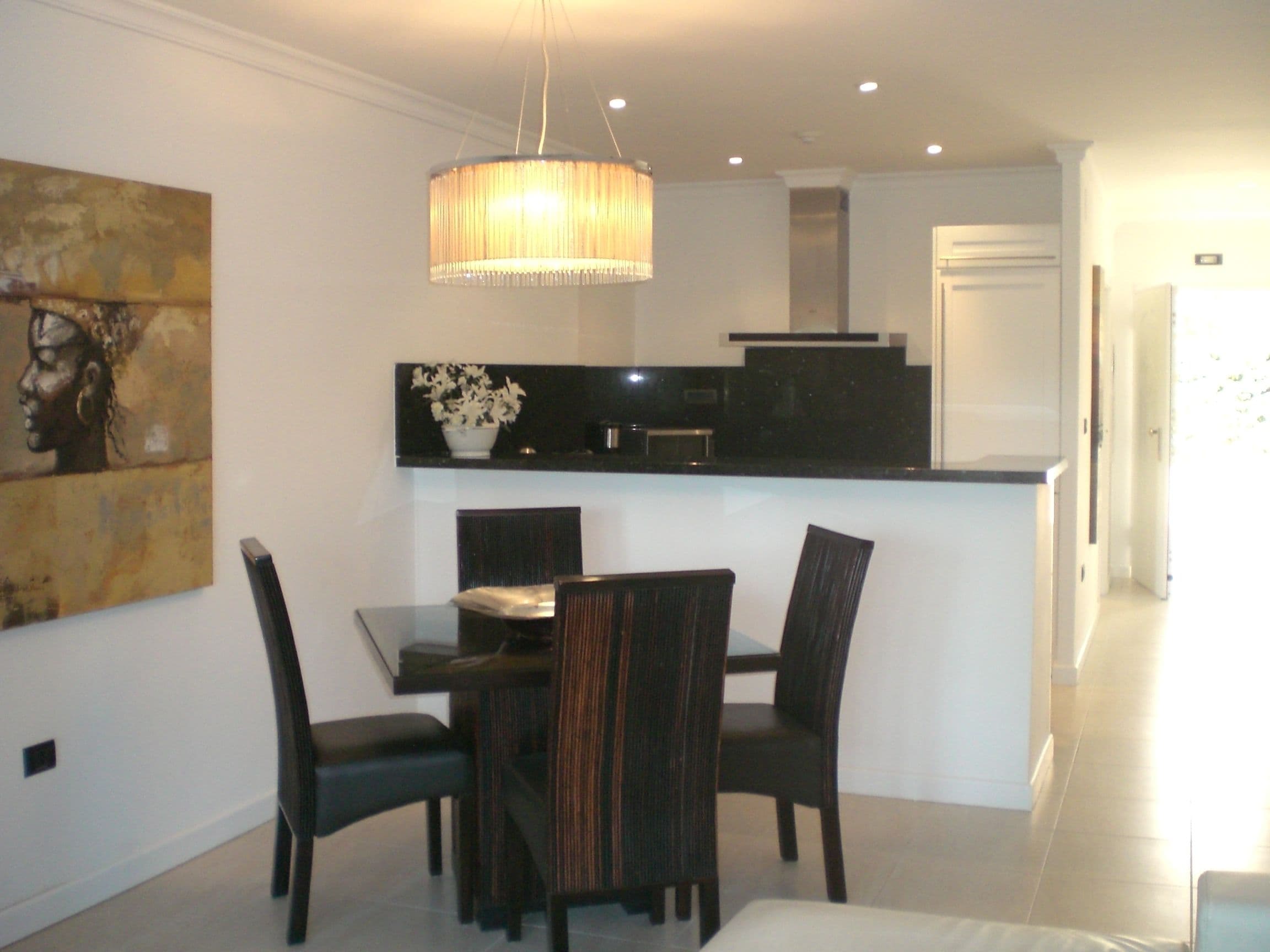 A modern dining area with a table and chairs, a pendant light, and a painting on the wall.