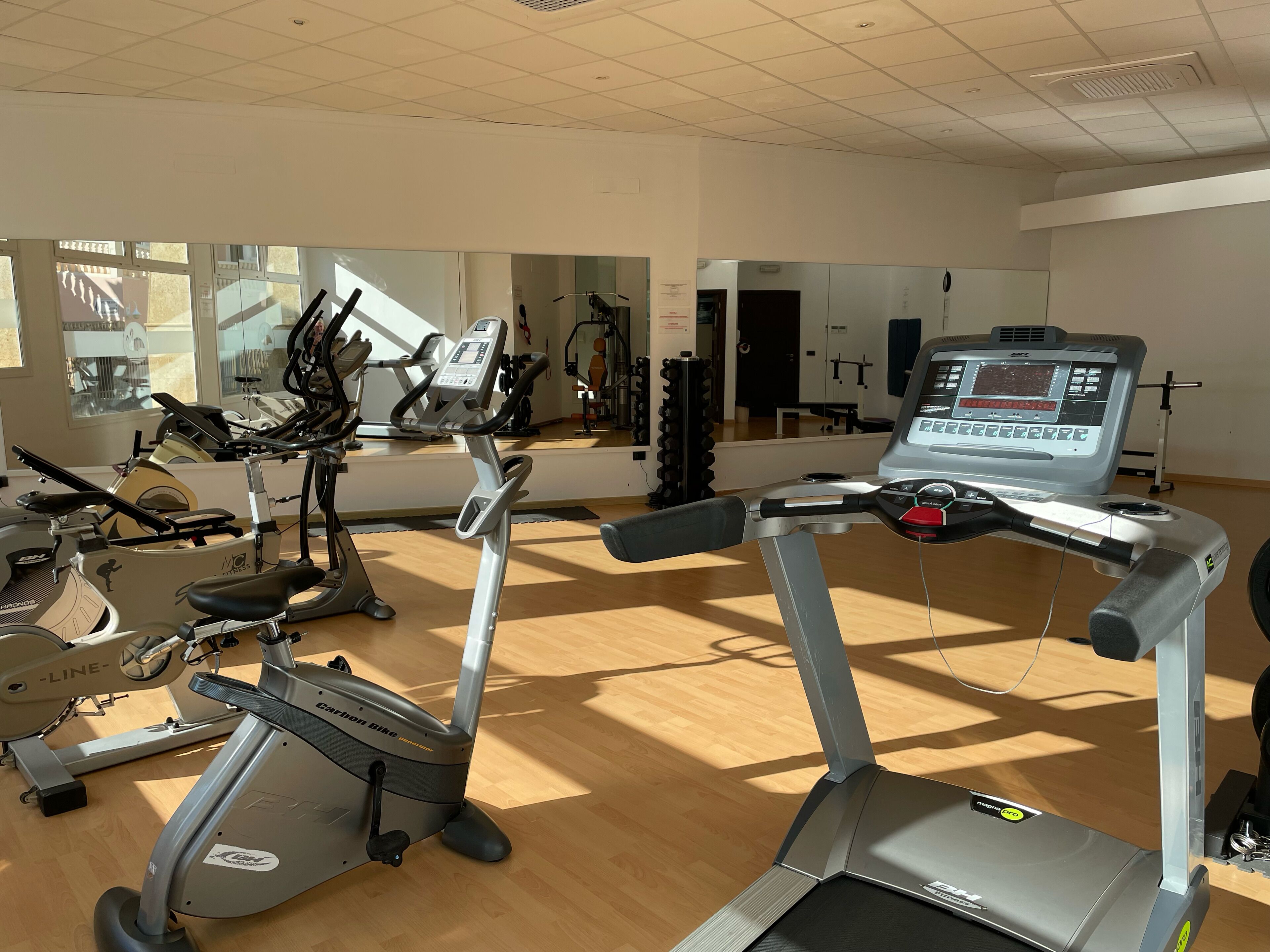 A gym with various exercise equipment, including treadmills and stationary bikes, and a large mirror on the wall.