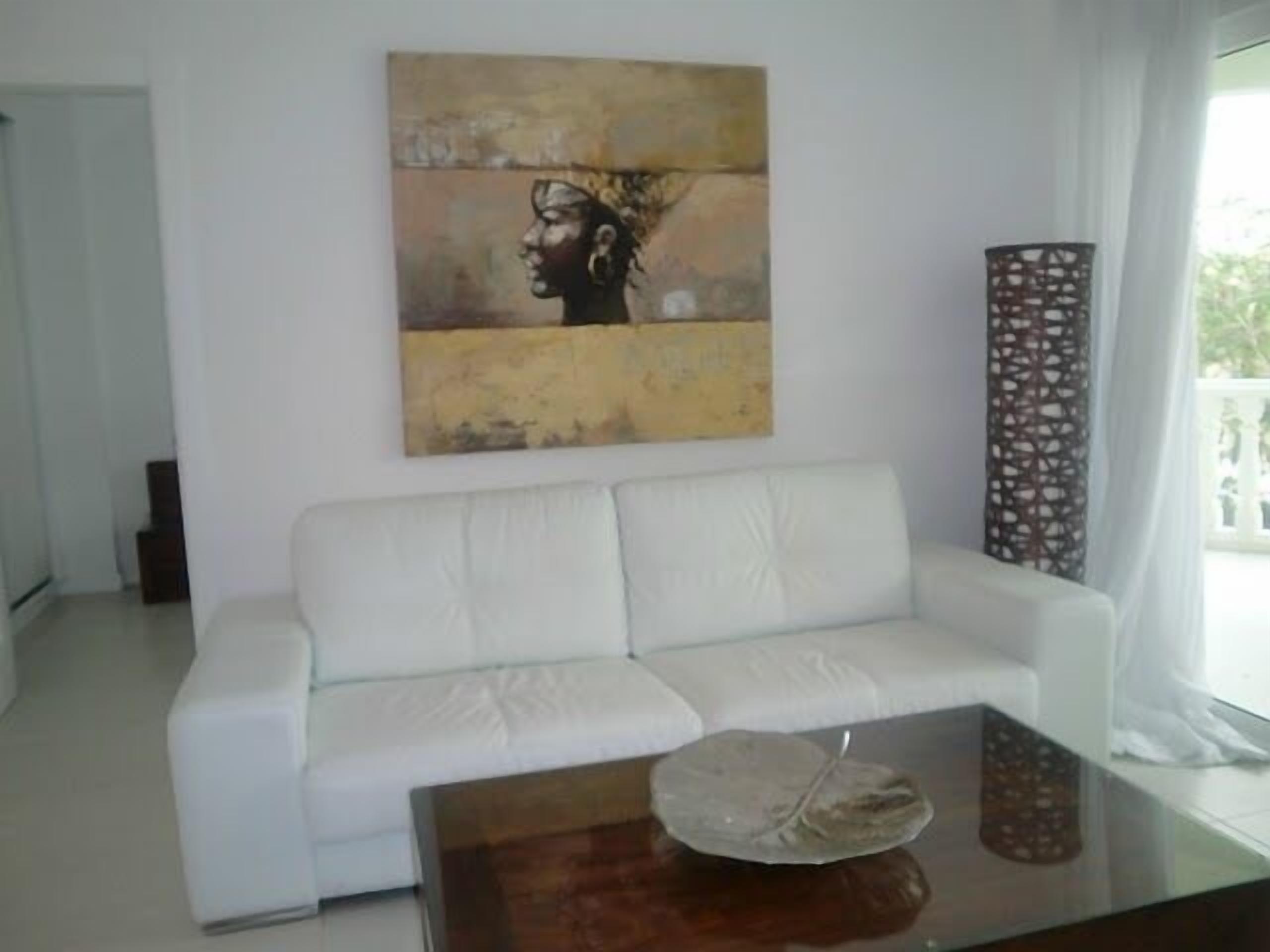 A white sofa, a glass coffee table with a decorative item, and a large abstract painting on the wall.