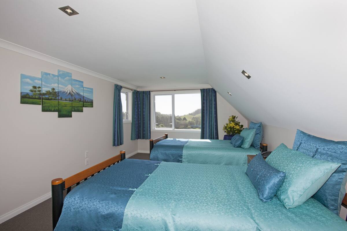 A bedroom with two beds, a large window with curtains, and a wall painting.