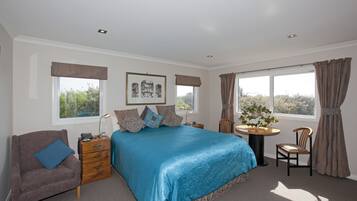 A bedroom with a large bed, a bedside table with a lamp, a chair, and a small table with a plant.