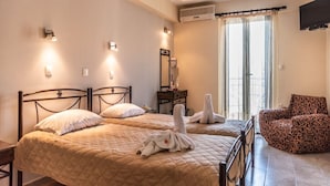 A hotel room with two beds, a sitting area with a patterned chair, and a TV mounted on the wall. - Matina Hotel (Samos)