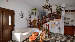 A living room with a white sofa, wooden stools, a staircase, and a chandelier. - Matina Hotel (Samos)