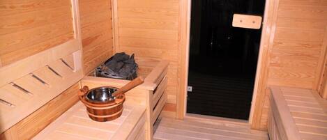 A sauna room with wooden walls, a bench, a wooden bowl, and a towel rack.