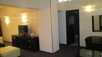 Ein Hotelzimmer mit einem Flachbildfernseher auf einer dunklen Holzkommode, einem weißen Hocker, einem Glastisch und einem Spiegel an der Wand.