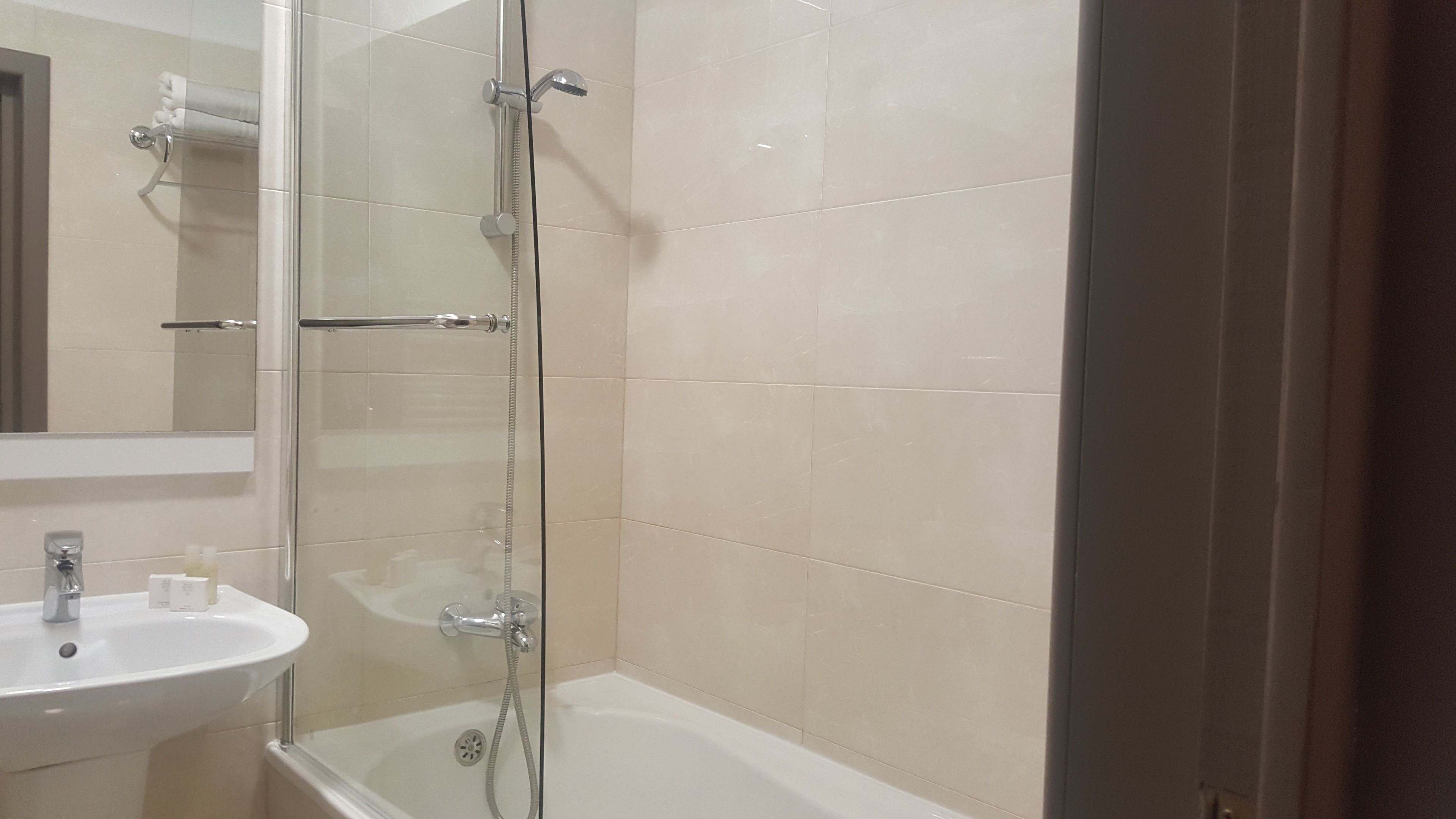 Een badkamer met een douchecabine van glas, een witte wastafel en een bad.