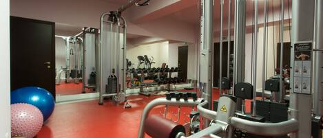 Un gimnasio con equipo de ejercicio, piso rojo y un espejo que refleja la sala.