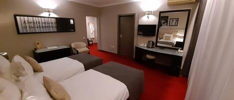 Ein Hotelzimmer mit zwei Betten, einem Schreibtisch, einem Sessel, einem Fernseher und einem Spiegel.