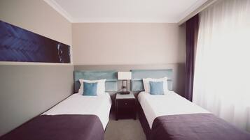 A hotel room with two beds, a nightstand, a lamp, and a painting on the wall.