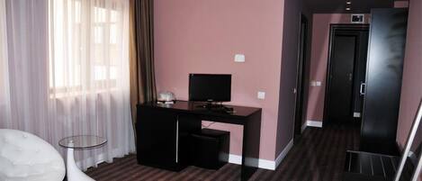 Een hotelkamer met een zwart bureau, een witte stoel, een glazen tafel en een groot raam met transparante gordijnen.