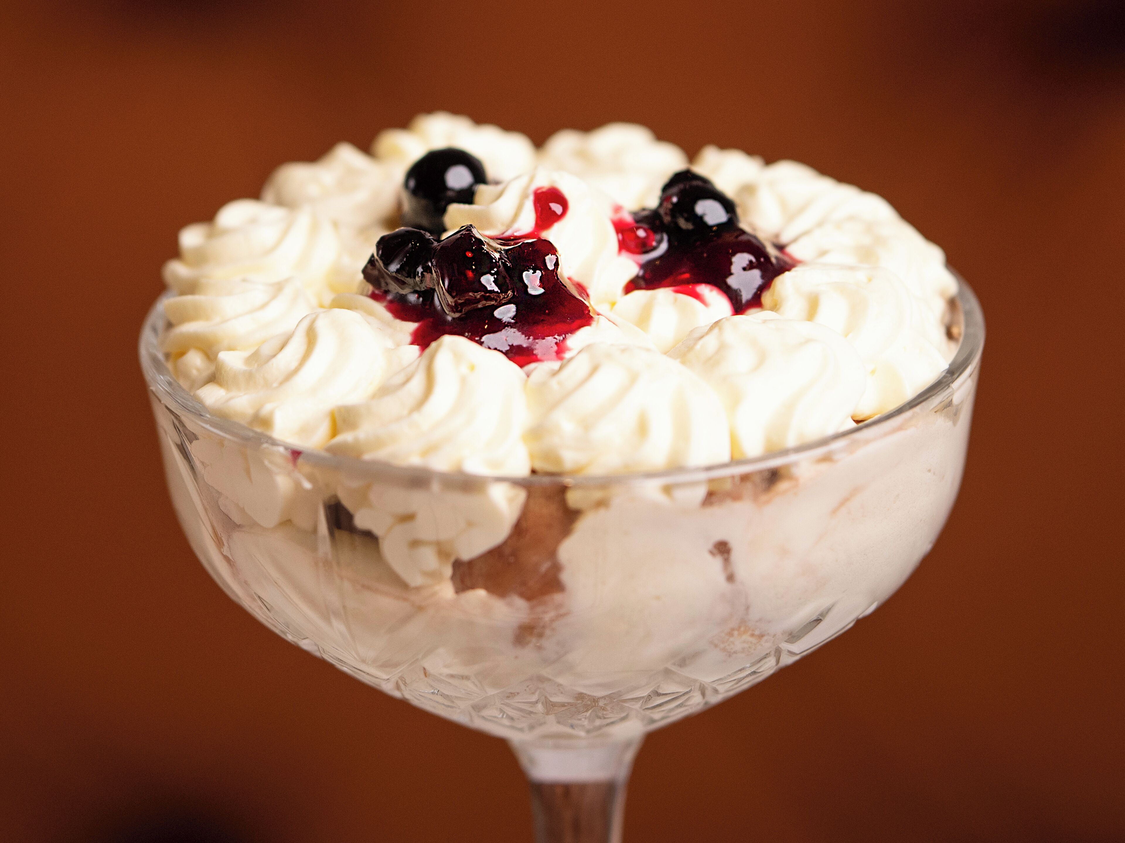 A dessert in a clear glass bowl with whipped cream and berries.