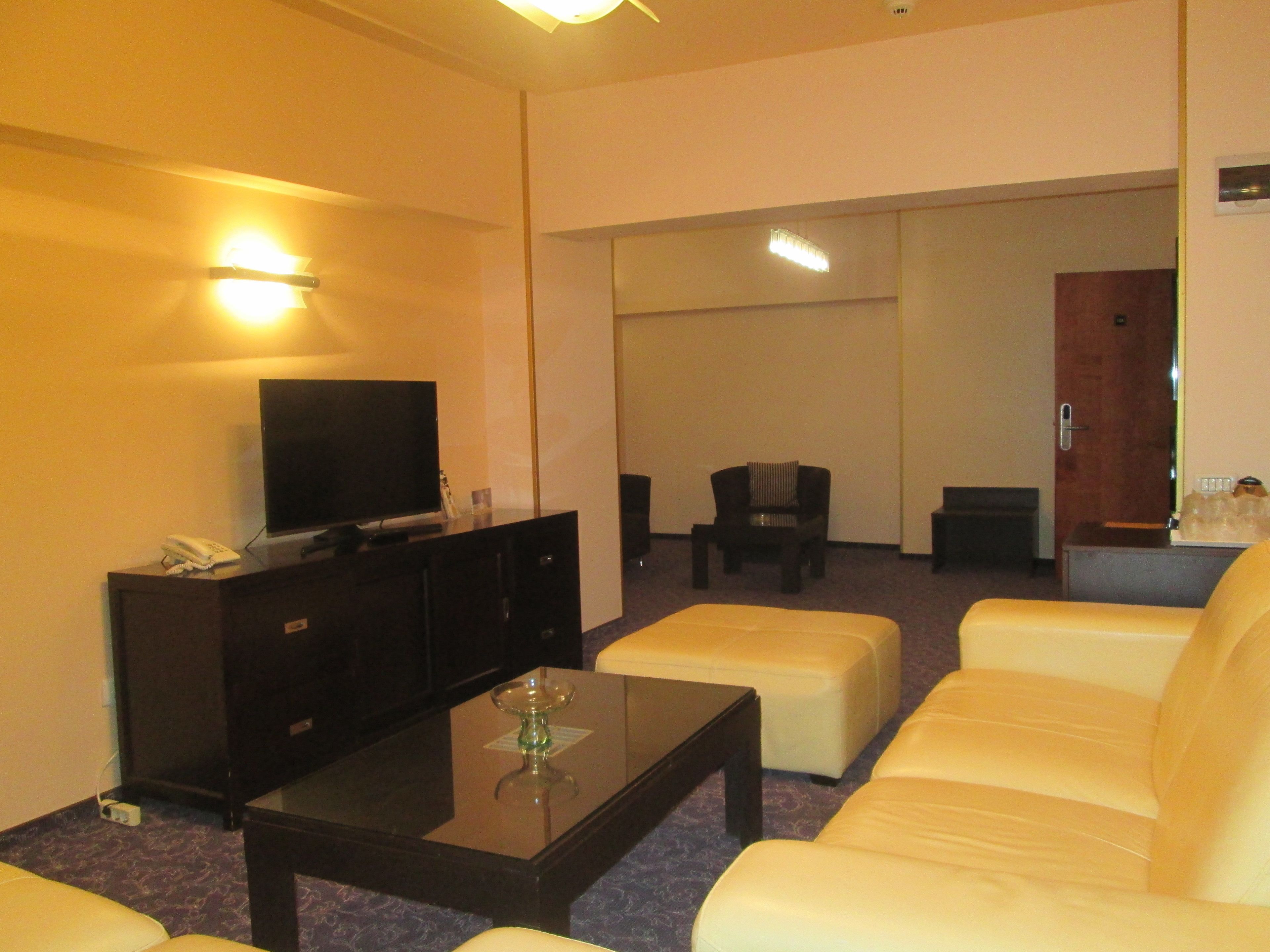 A hotel room with a flat-screen TV on a cabinet, a sofa, a coffee table, and a chair.