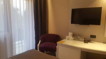 Une chambre d’hôtel comprenant un lit, un bureau, une chaise, un téléviseur fixé au mur et une fenêtre avec des rideaux.