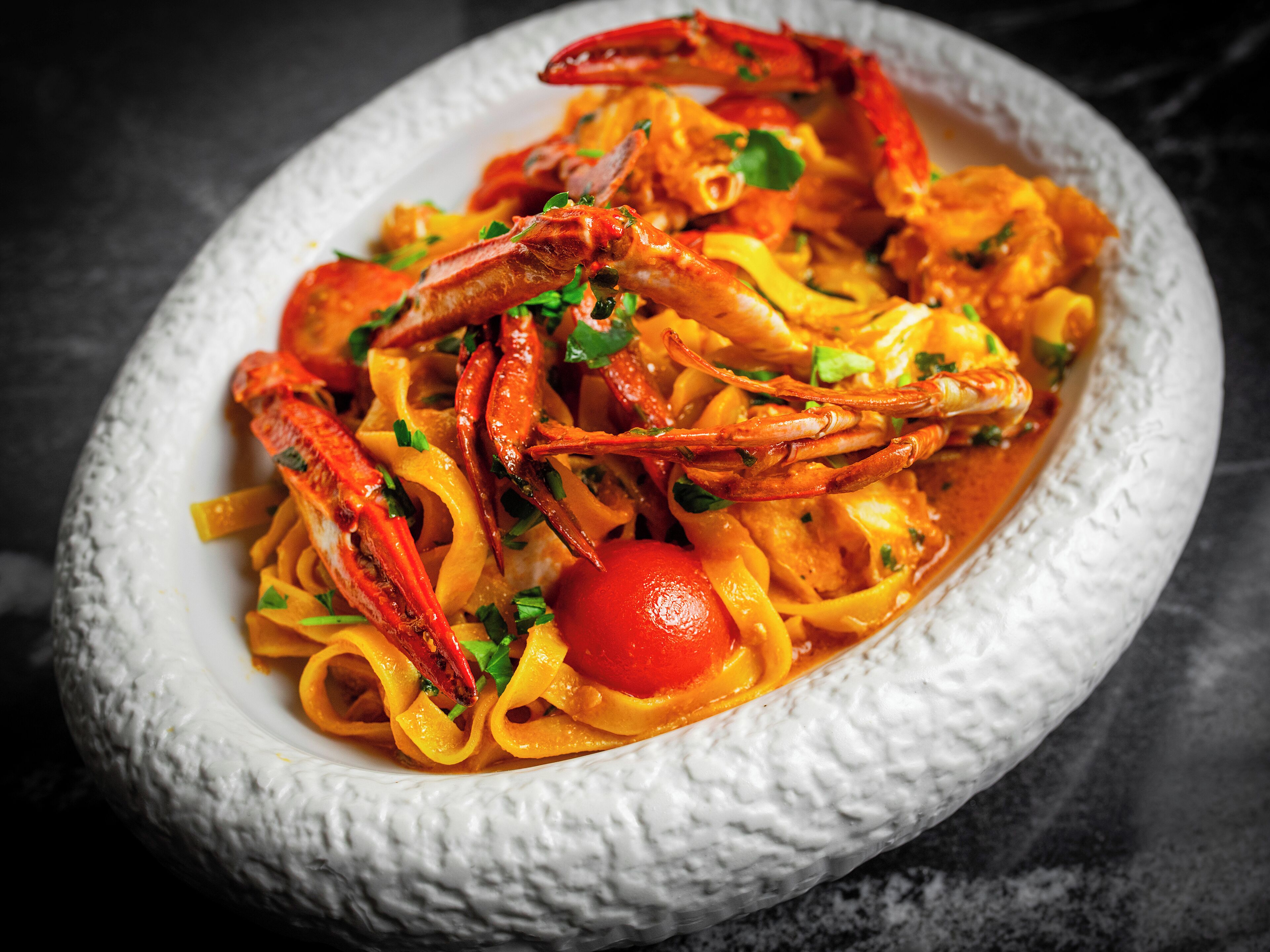 A dish of pasta with shrimp and vegetables in a white bowl.