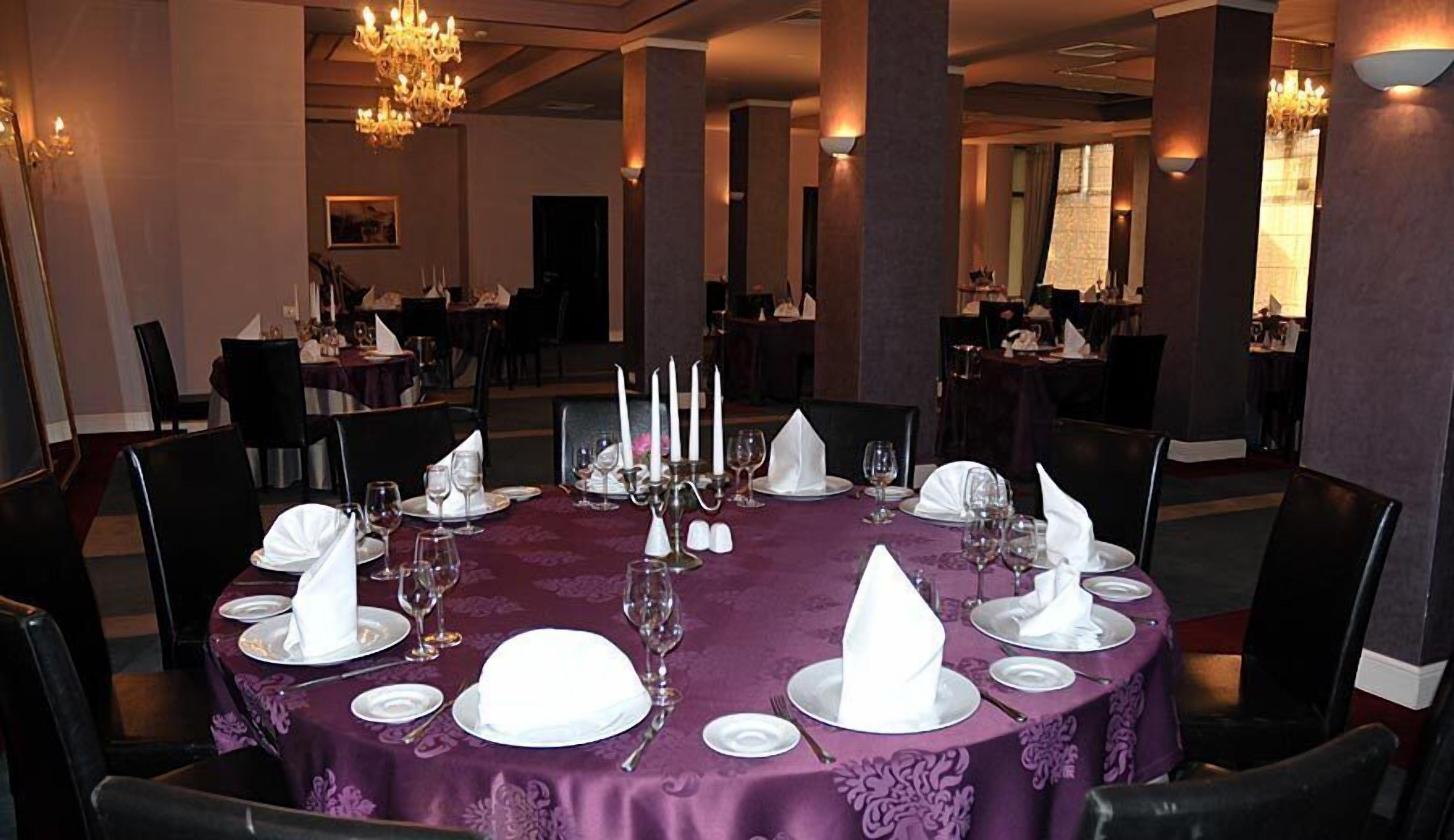 Un comedor formal con mesas redondas dispuestas para una comida, con servilletas blancas, copas de vino y candelabros.