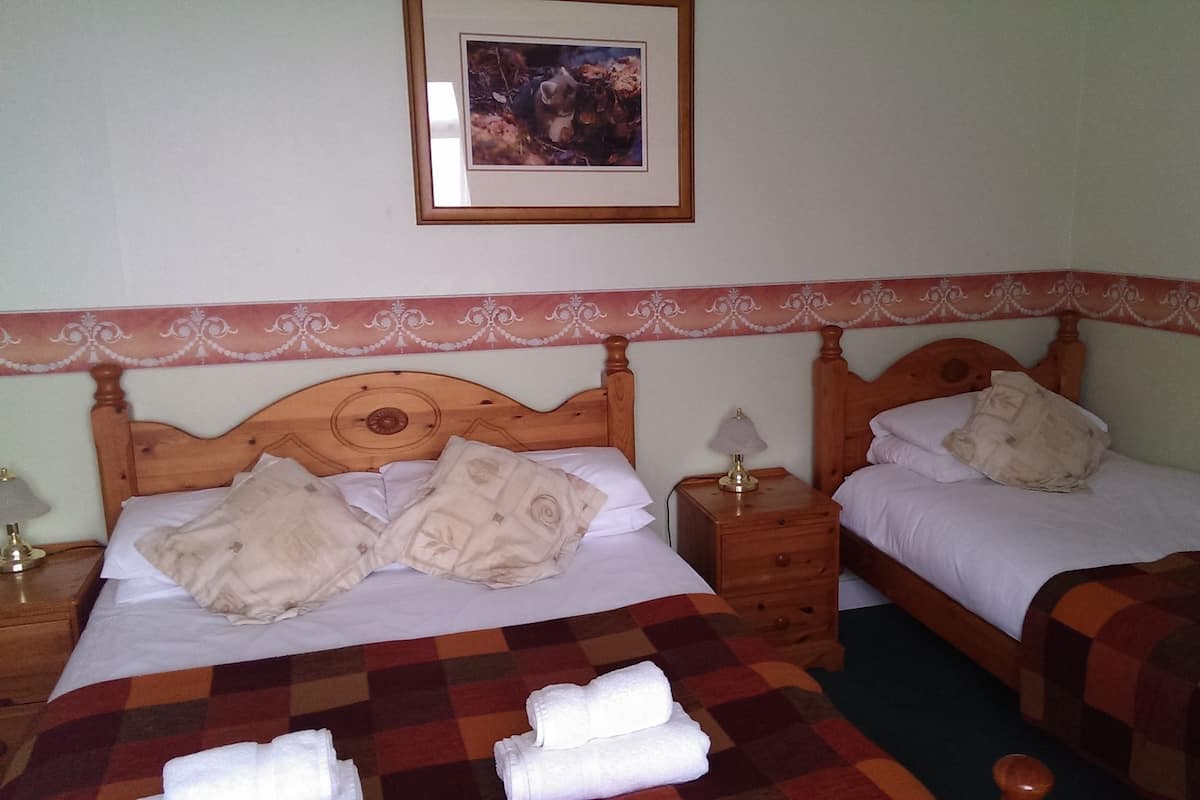 A hotel room with two beds, a nightstand with a lamp, and a framed picture on the wall.