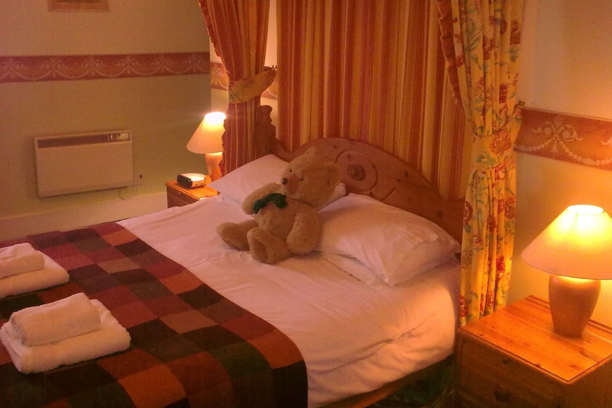A hotel room with a bed, two bedside lamps, a heater, and a checkered blanket.