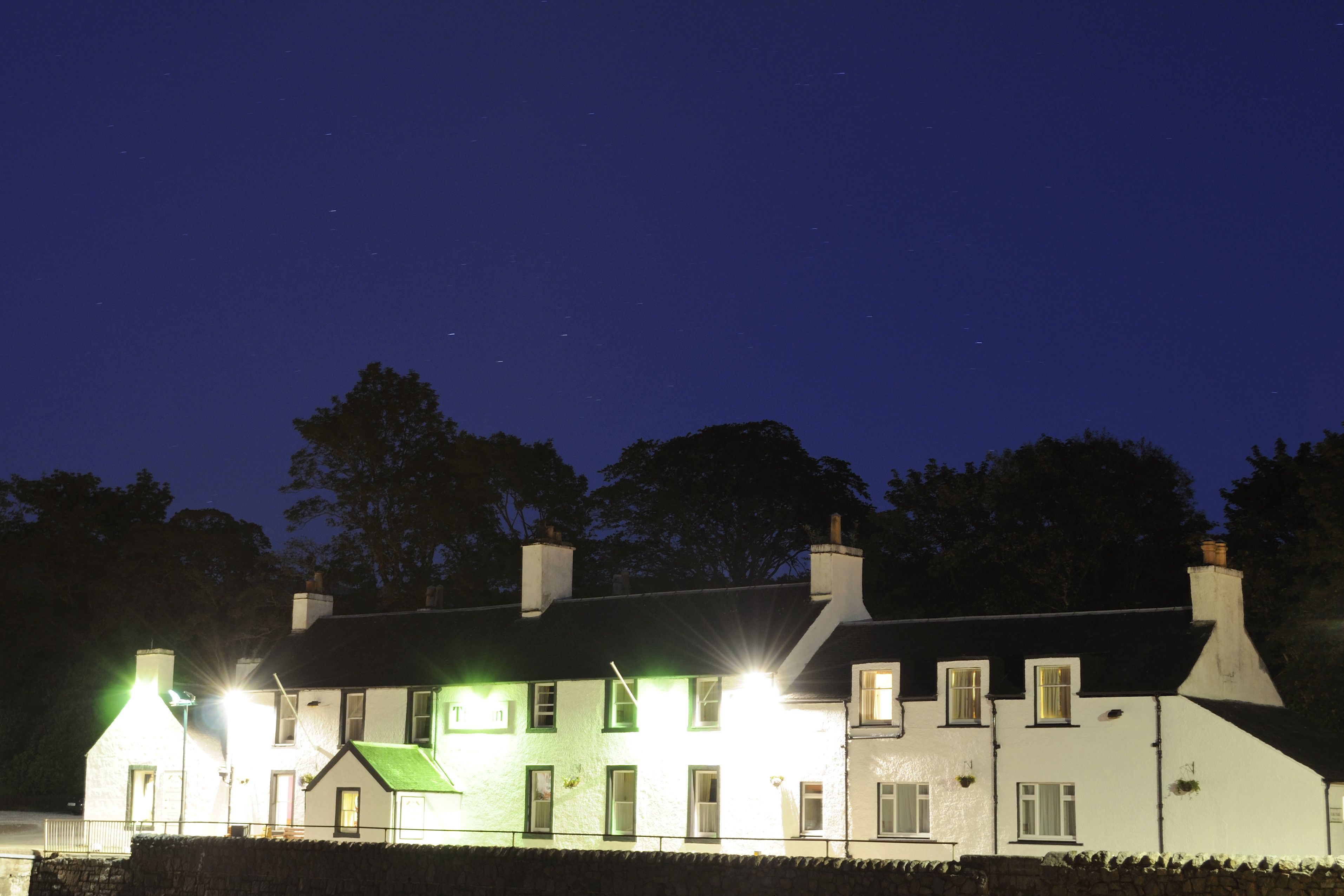 A two-story building with multiple windows and a green roof, illuminated by exterior lights at night.