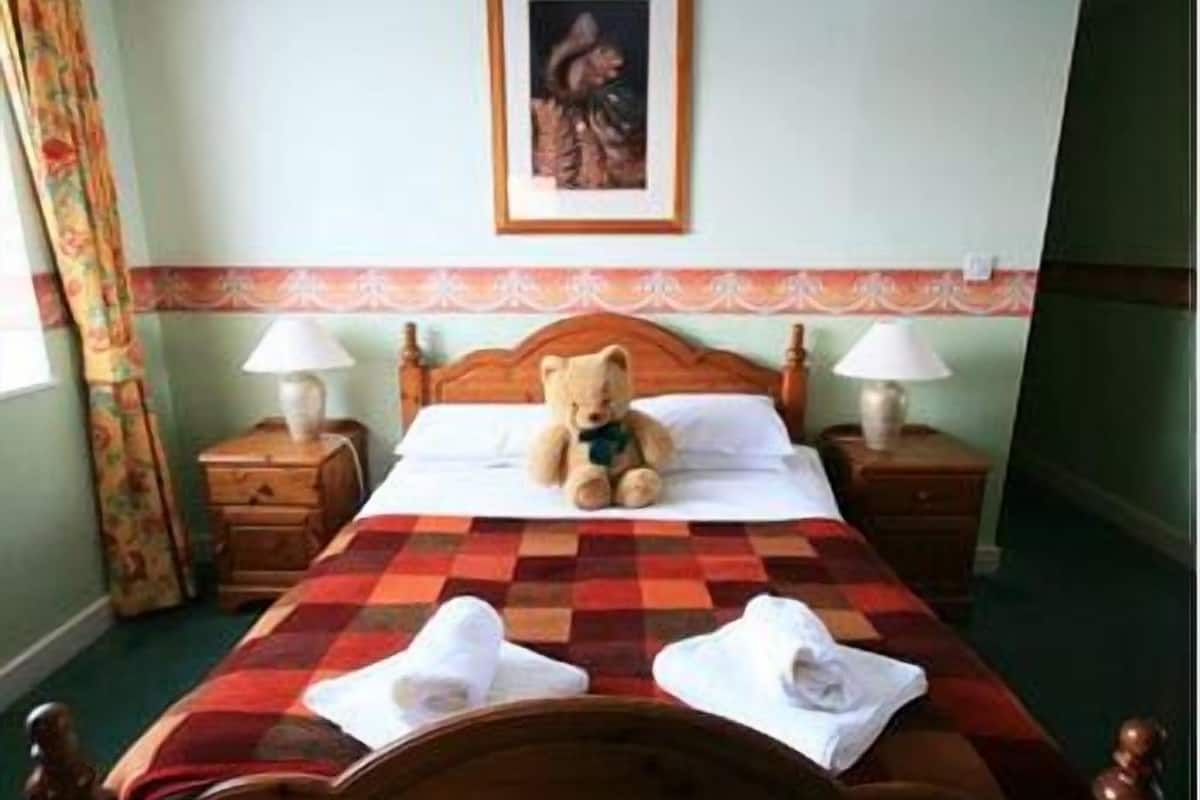 A neatly made bed with a checkered bedspread, two bedside lamps, and a teddy bear on the bed.