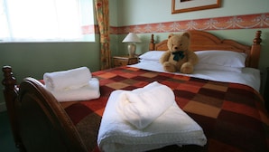 A neatly made bed with a checkered bedspread, two towels on the side, and a teddy bear on the pillows.