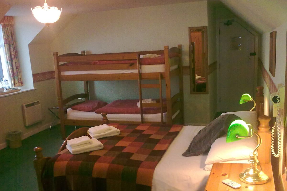 A bunk bed with a checkered blanket, a bedside table with a lamp, and a mirror on the wall.