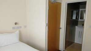 Una camera d'albergo con un letto, una porta in legno, un bagno con lavandino e specchio, e un angolo cottura.