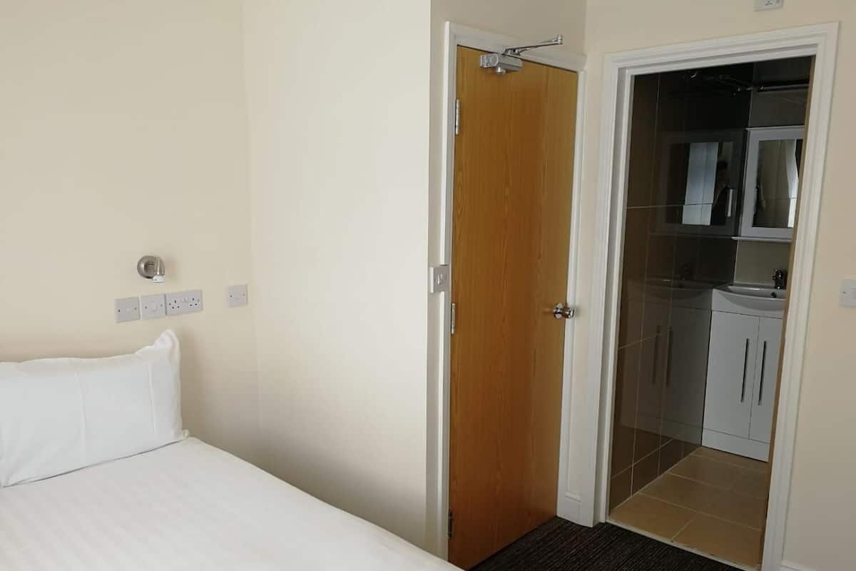 A hotel room with a bed, a wooden door, a bathroom with a sink and mirror, and a small kitchenette.