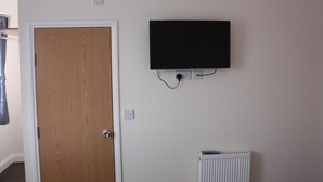 Una stanza con una porta in legno, un termosifone bianco e una TV a schermo piatto montata al muro.