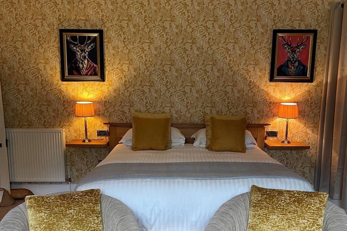 A double bed with two gold pillows, a headboard, and two wall-mounted lamps.