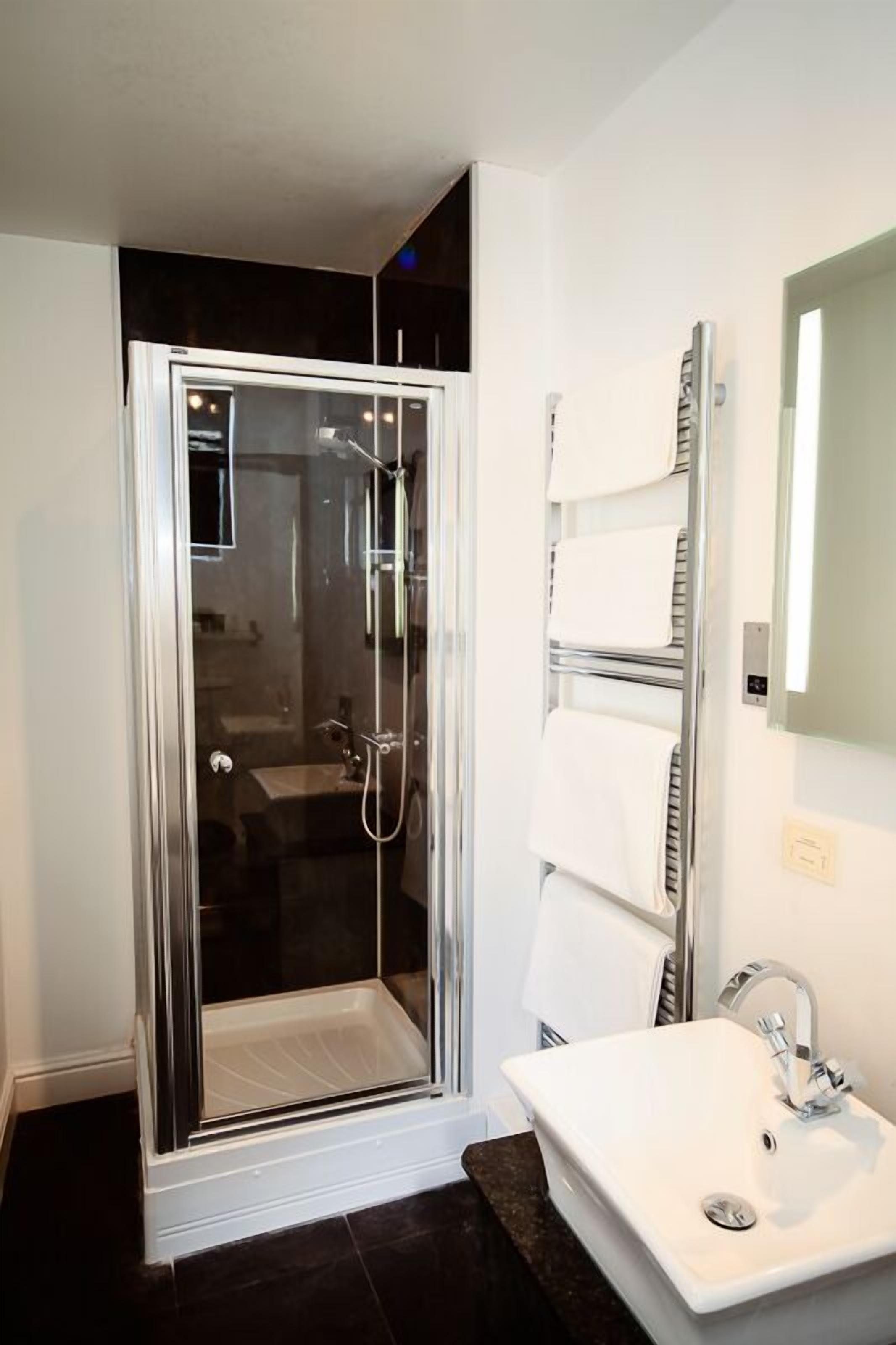 A modern bathroom with a glass-enclosed shower, a white sink with a mirror, and a towel rack with multiple towels.