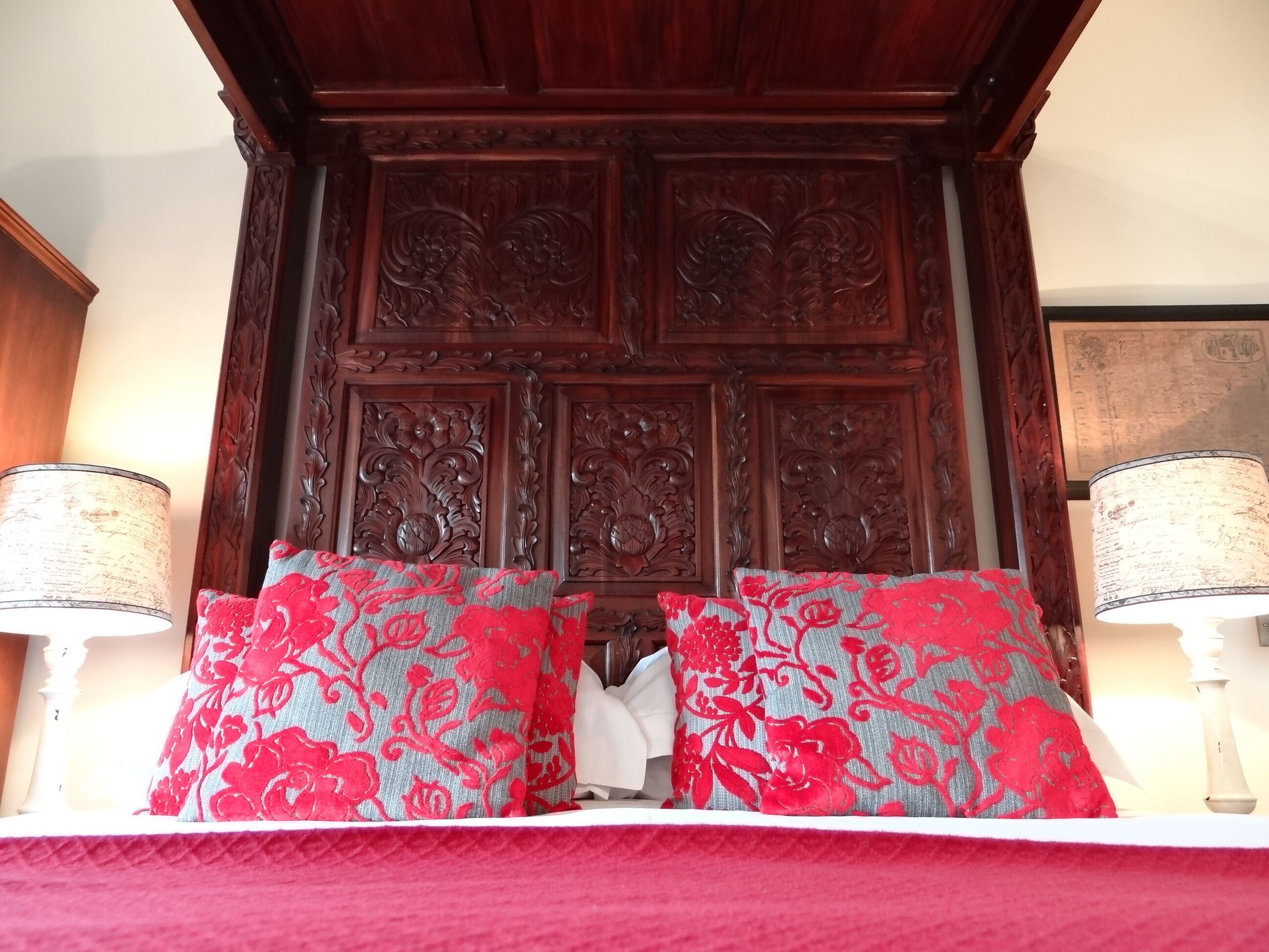 A bed with red floral pillows, a wooden headboard with intricate carvings, and two bedside lamps.