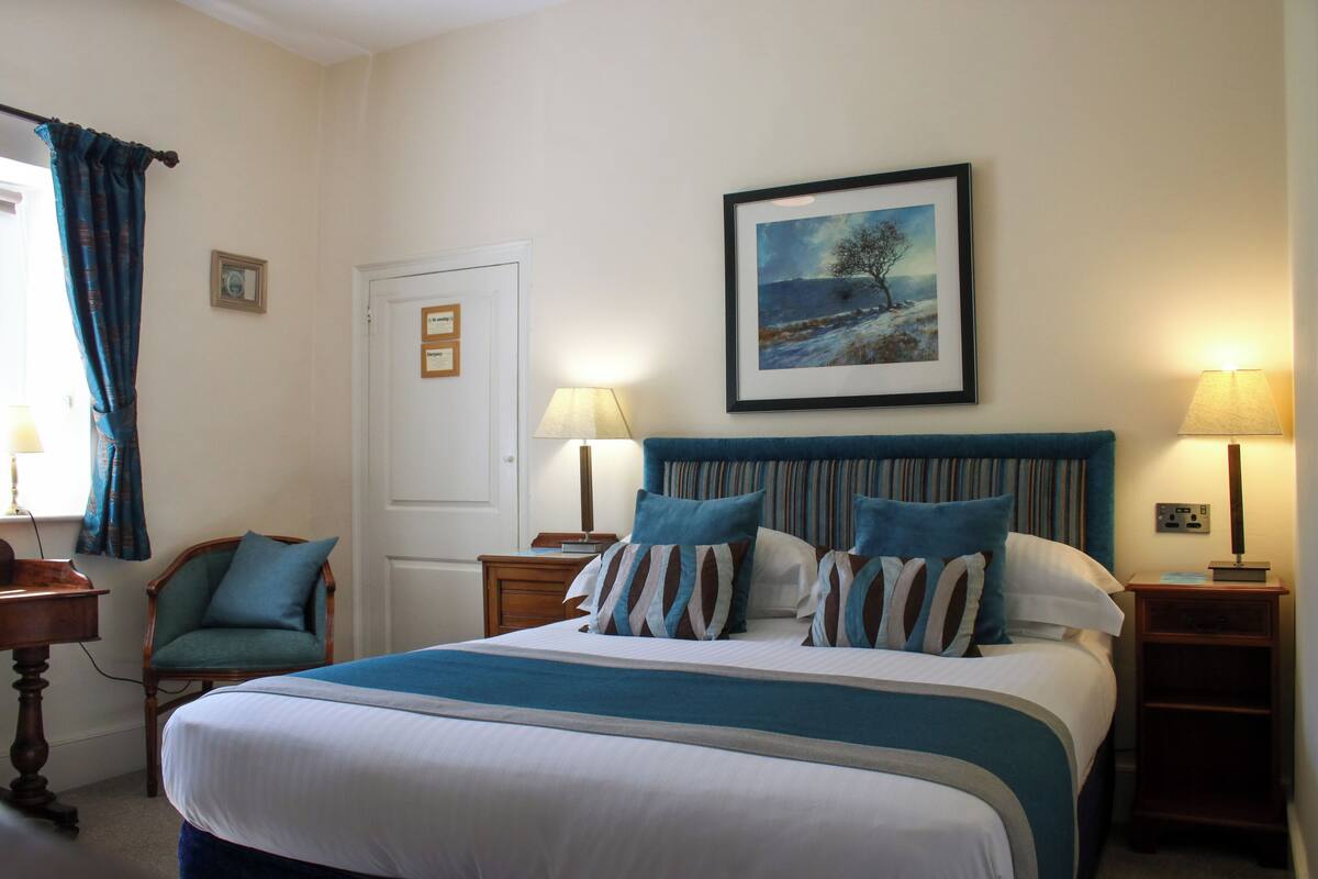 A neatly arranged bedroom with a large bed, two bedside tables with lamps, a chair, and a door.