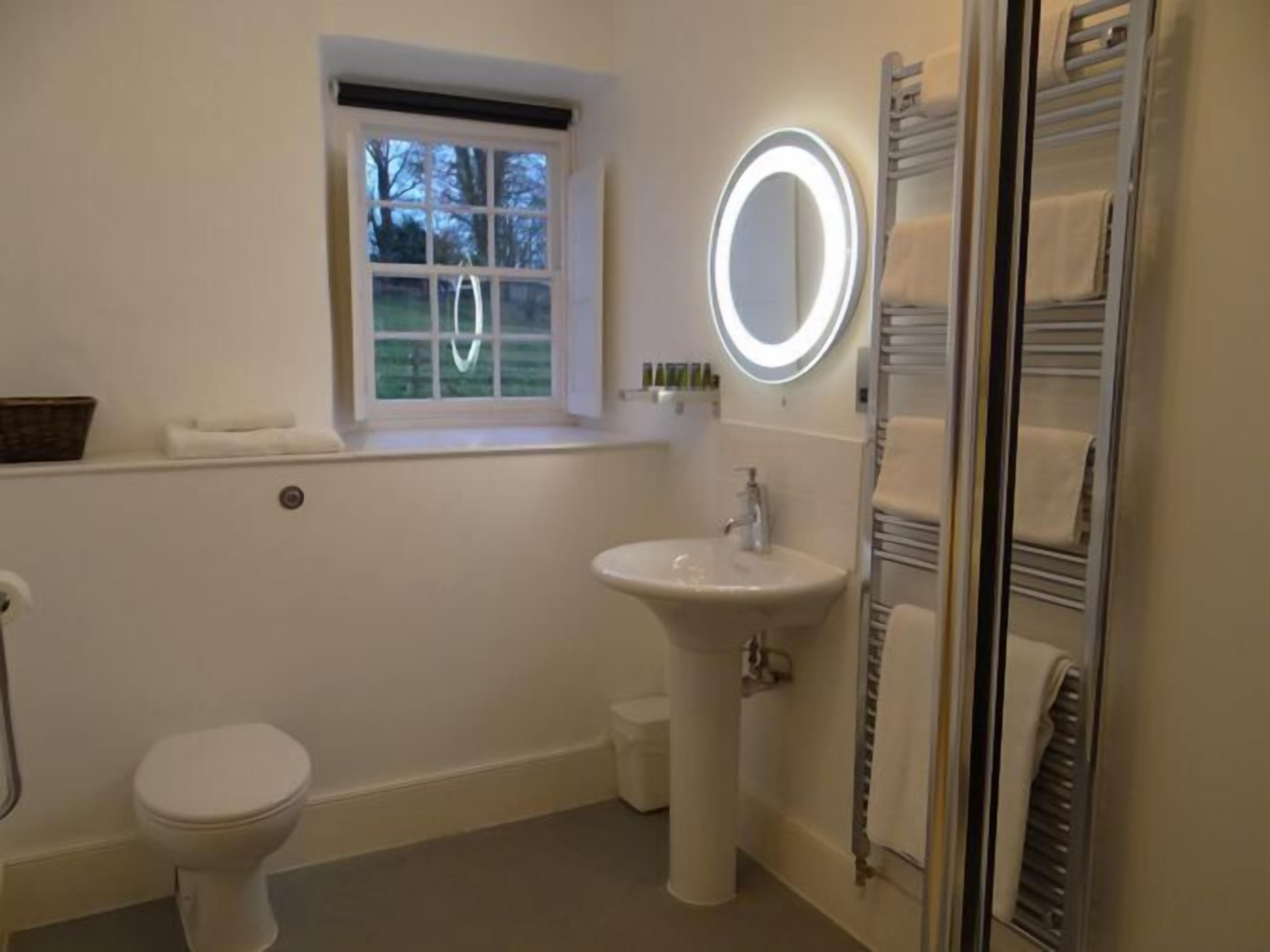 Un baño con inodoro, lavamanos con espejo, ventana y toallero.