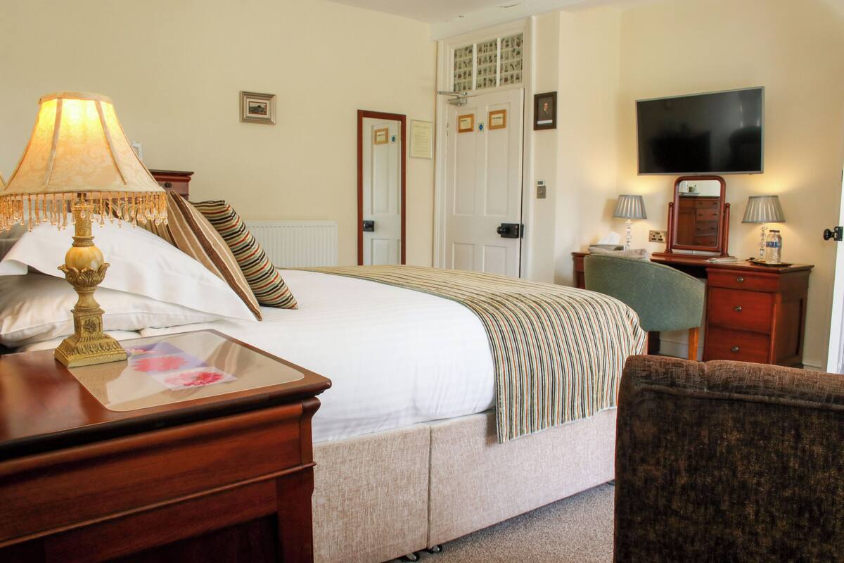 A hotel room with a bed, a desk with a lamp, a chair, a television, and a dresser.