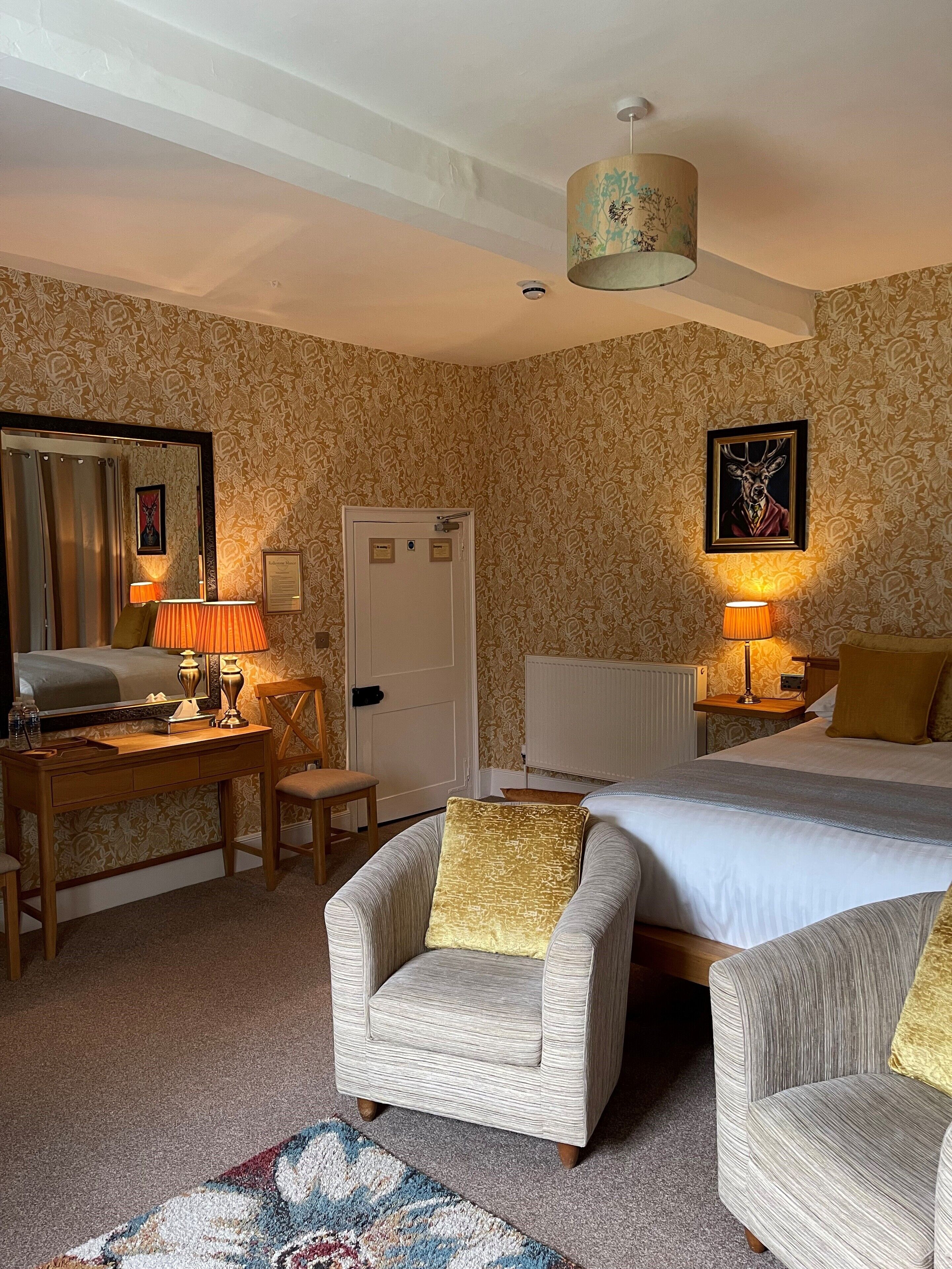 A hotel room with a bed, two armchairs, a desk, and a mirror.