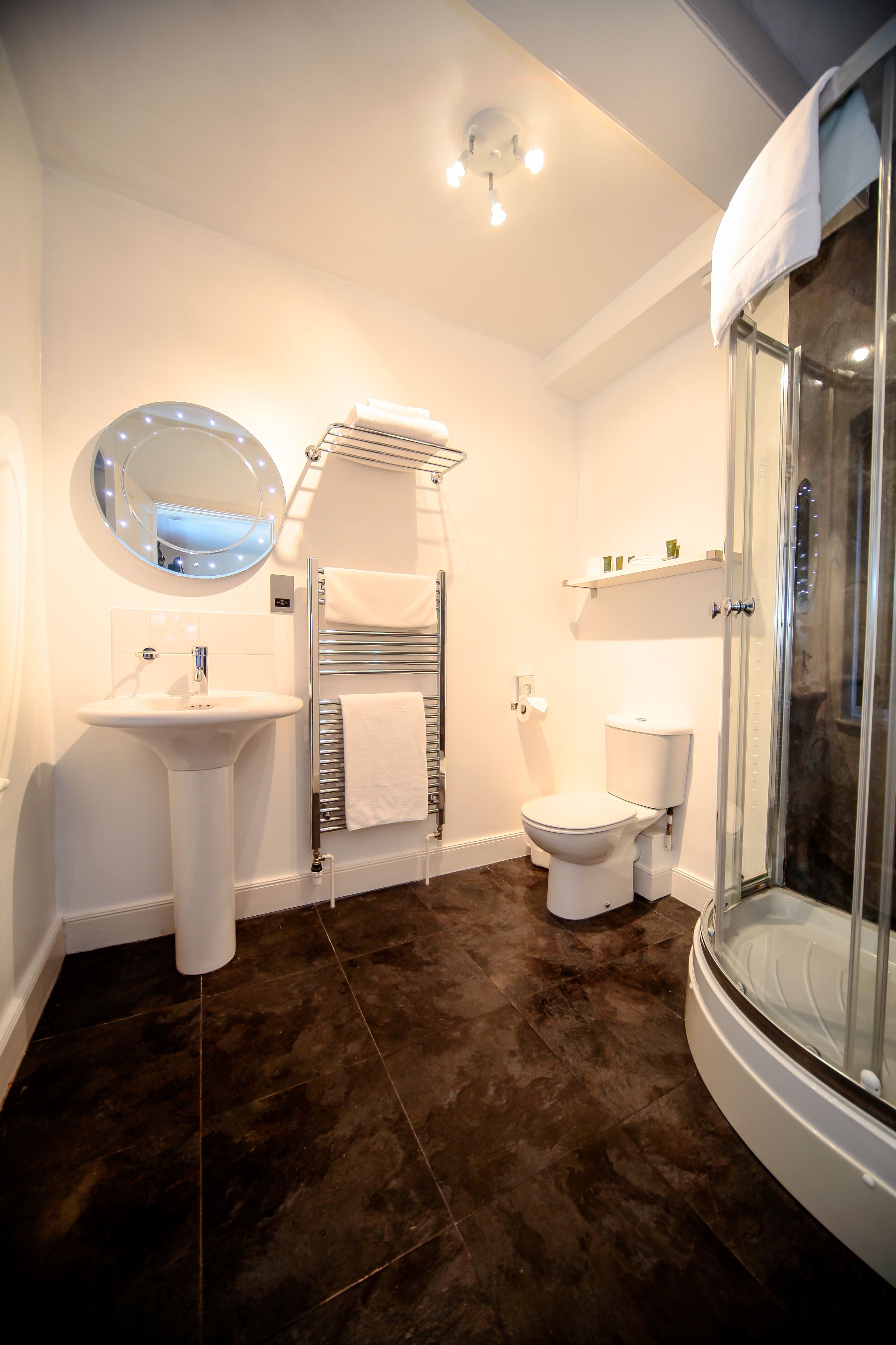 Un baño moderno con lavamanos pedestal, inodoro y ducha con mampara de vidrio.