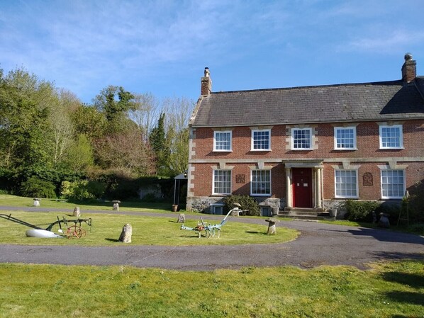 A two-story brick house with a red door, multiple windows, and a well-maintained lawn with garden sculptures.