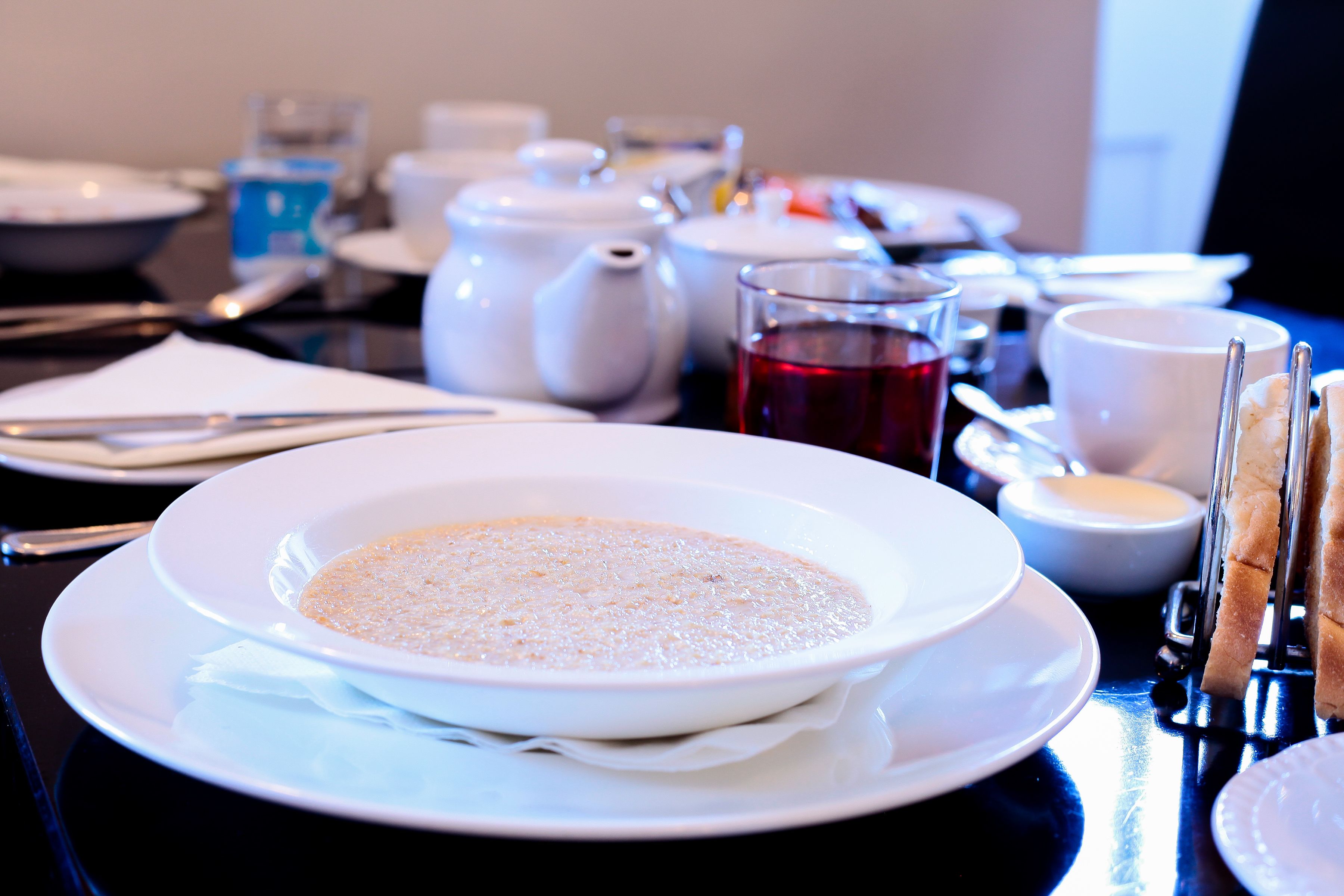 Una mesa de comedor dispuesta con un plato blanco de sopa, una tetera, tazas y un vaso de bebida roja.