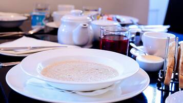 Una mesa de comedor dispuesta con un plato blanco de sopa, una tetera, tazas y un vaso de bebida roja.