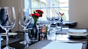 Una mesa de comedor dispuesta con varias copas de vino, un jarrón con flores rojas y un vaso de agua.