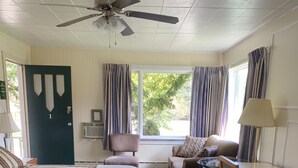 A hotel room with a bed, a desk, a chair, a ceiling fan, a window with curtains, and a door. - The Lionstone Inn Motel and Cottages (Pictou)