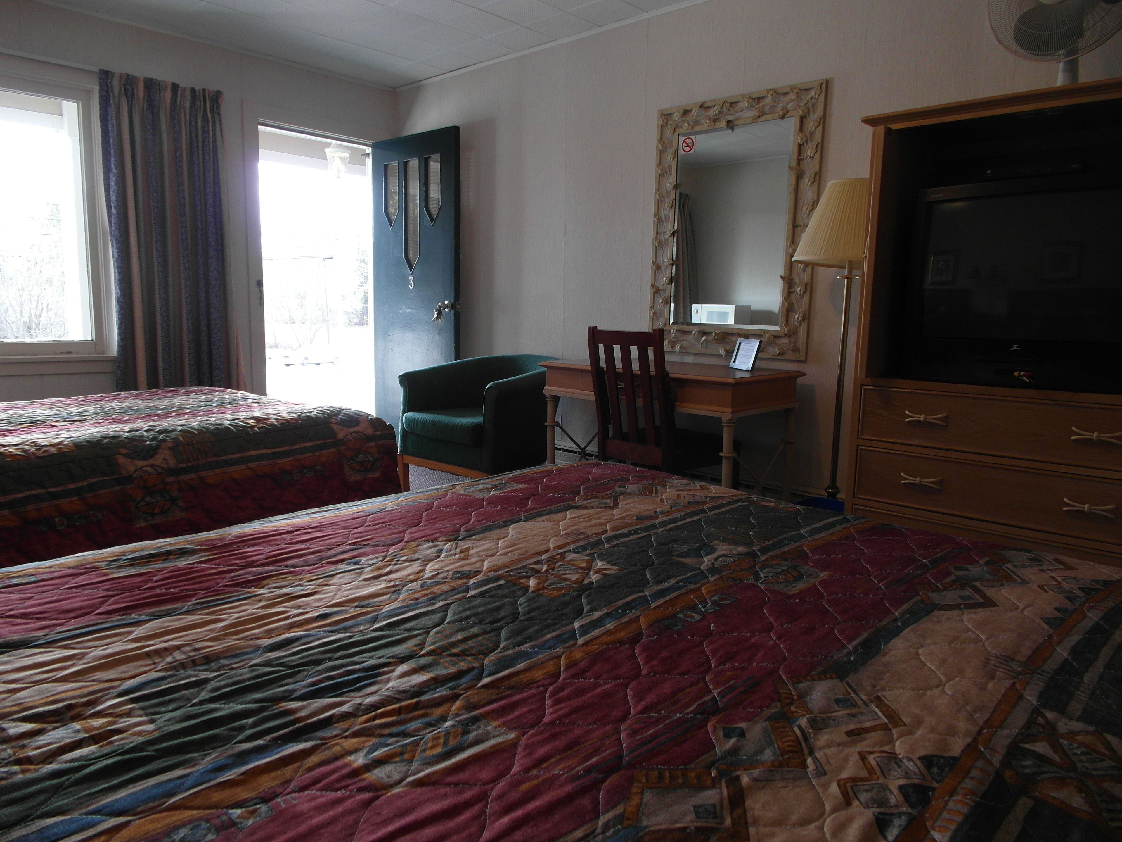 A hotel room with two beds, a desk, a chair, a dresser, and a large mirror.