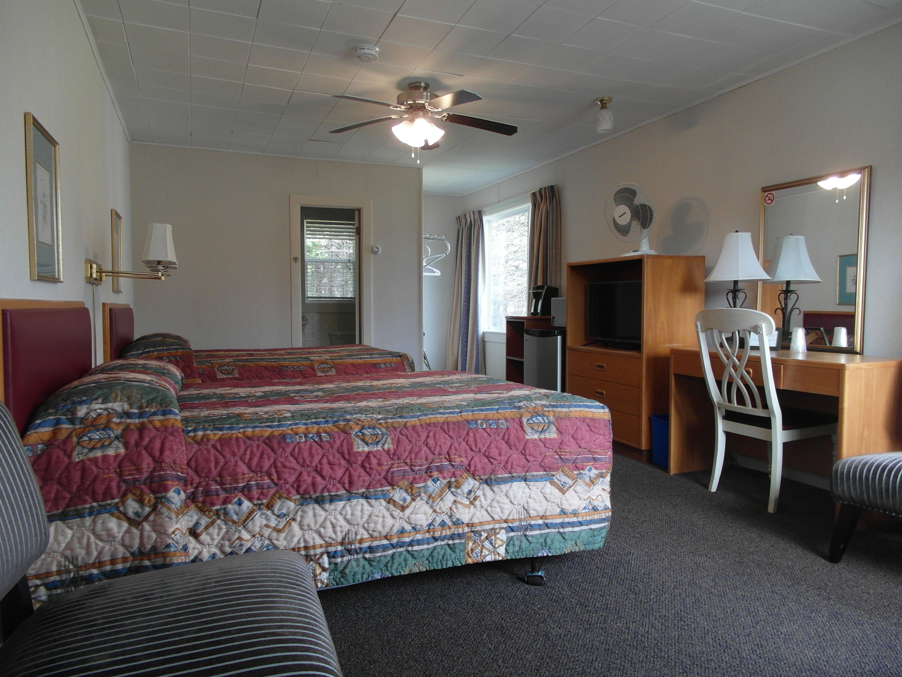 A hotel room with two beds, a desk, a chair, a ceiling fan, and a large mirror.