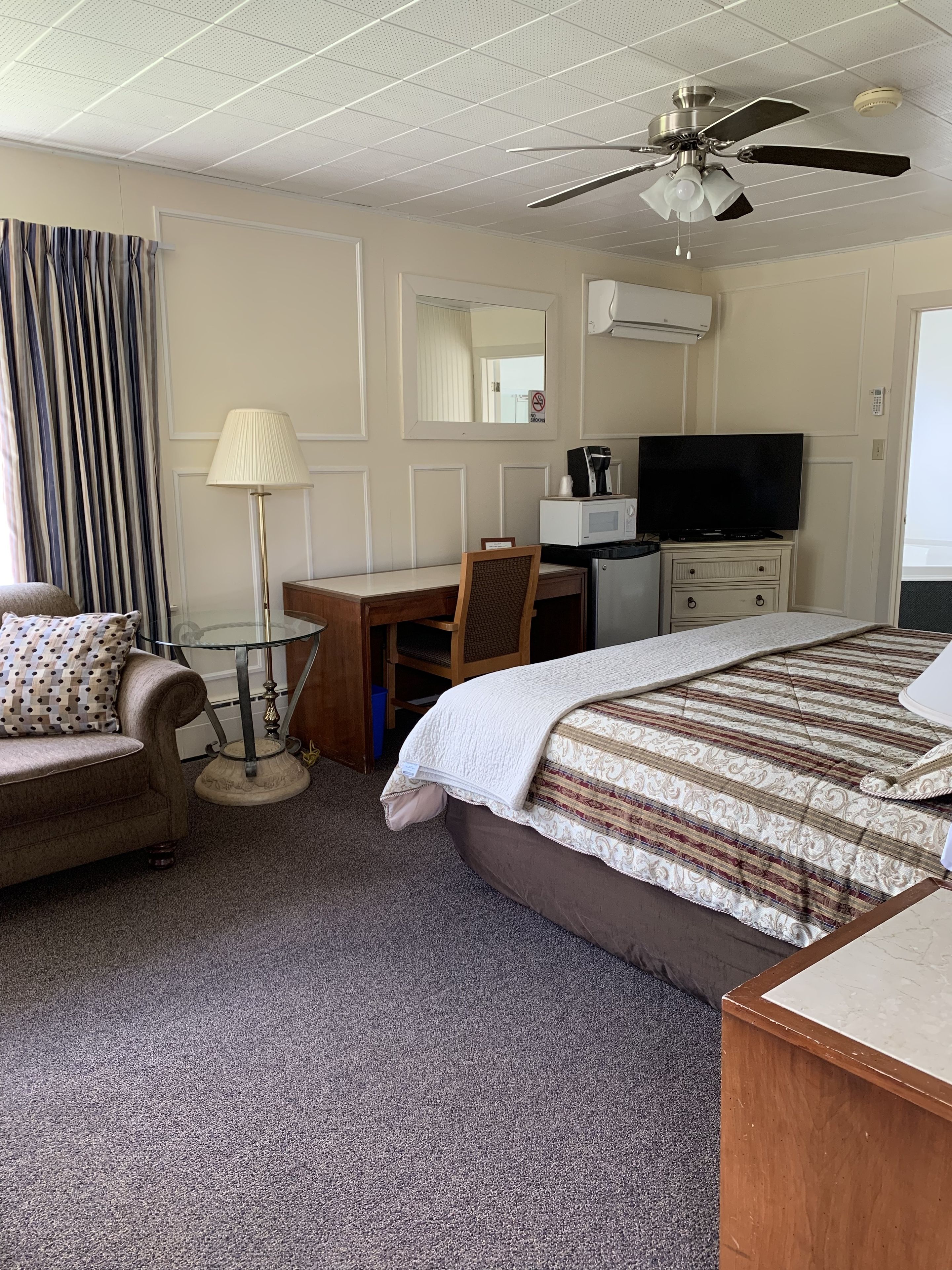 Een hotelkamer met een bed, een bureau, een stoel, een televisie en een plafondventilator.