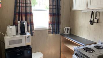A compact kitchenette with a microwave, toaster, kettle, and a small refrigerator.