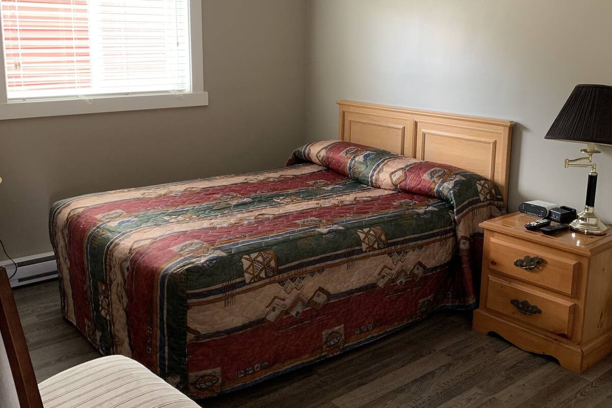 A bedroom with a bed, a nightstand, a chair, and a window with blinds.