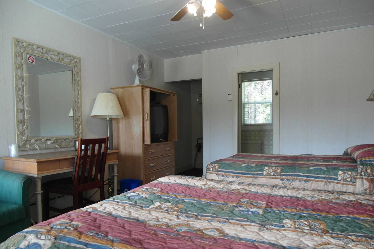 A bedroom with a bed, a desk, a chair, a dresser, a television, and a ceiling fan.