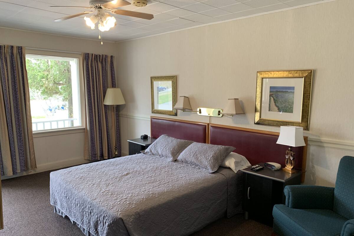 A hotel room with a bed, a desk, a chair, a ceiling fan, and two wall-mounted lamps.
